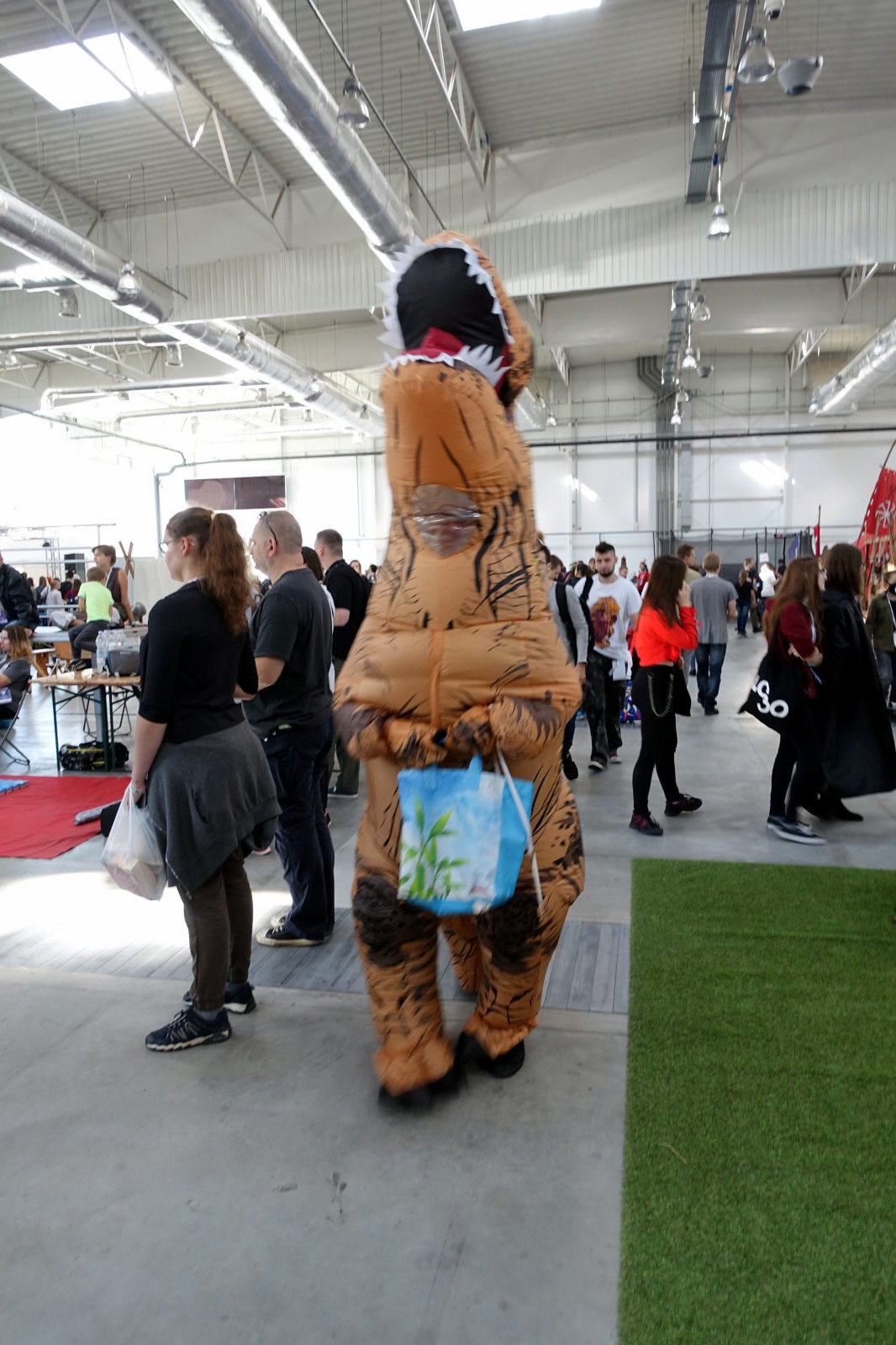 A person in an inflatable T-rex costume with a bag in their hands. There are multiple people around.