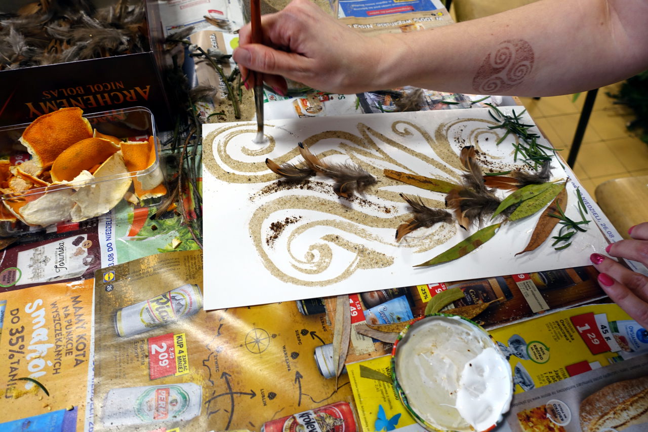 Picture shows a piece of art being prepared. There is a hand with a brush applying something on a piece of paper.