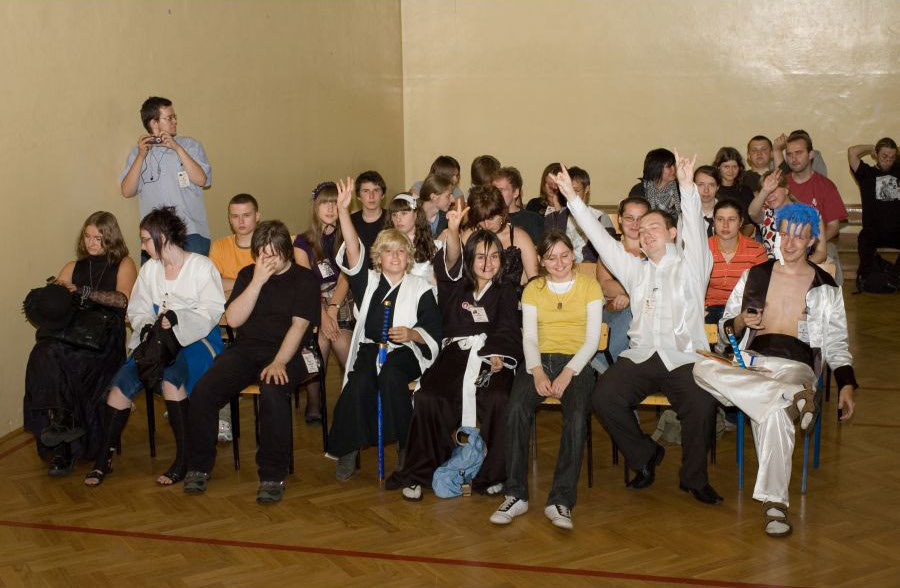 A group of people sitting on chairs in a large room. Some of them wear manga cosplay.