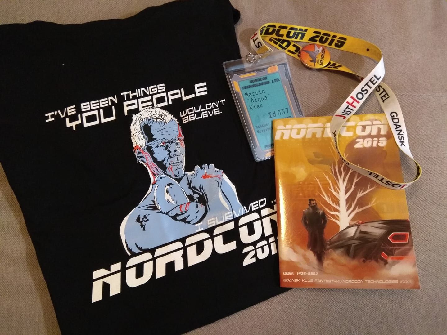 Convention t-shirt, badge with lanyard and Programme book. T-shirt shows a portrait inspired by Roy Batty from Blade runner movie and an inscription 'I've seen things you people wouldn't believe. I survived Nordcon 2019'.