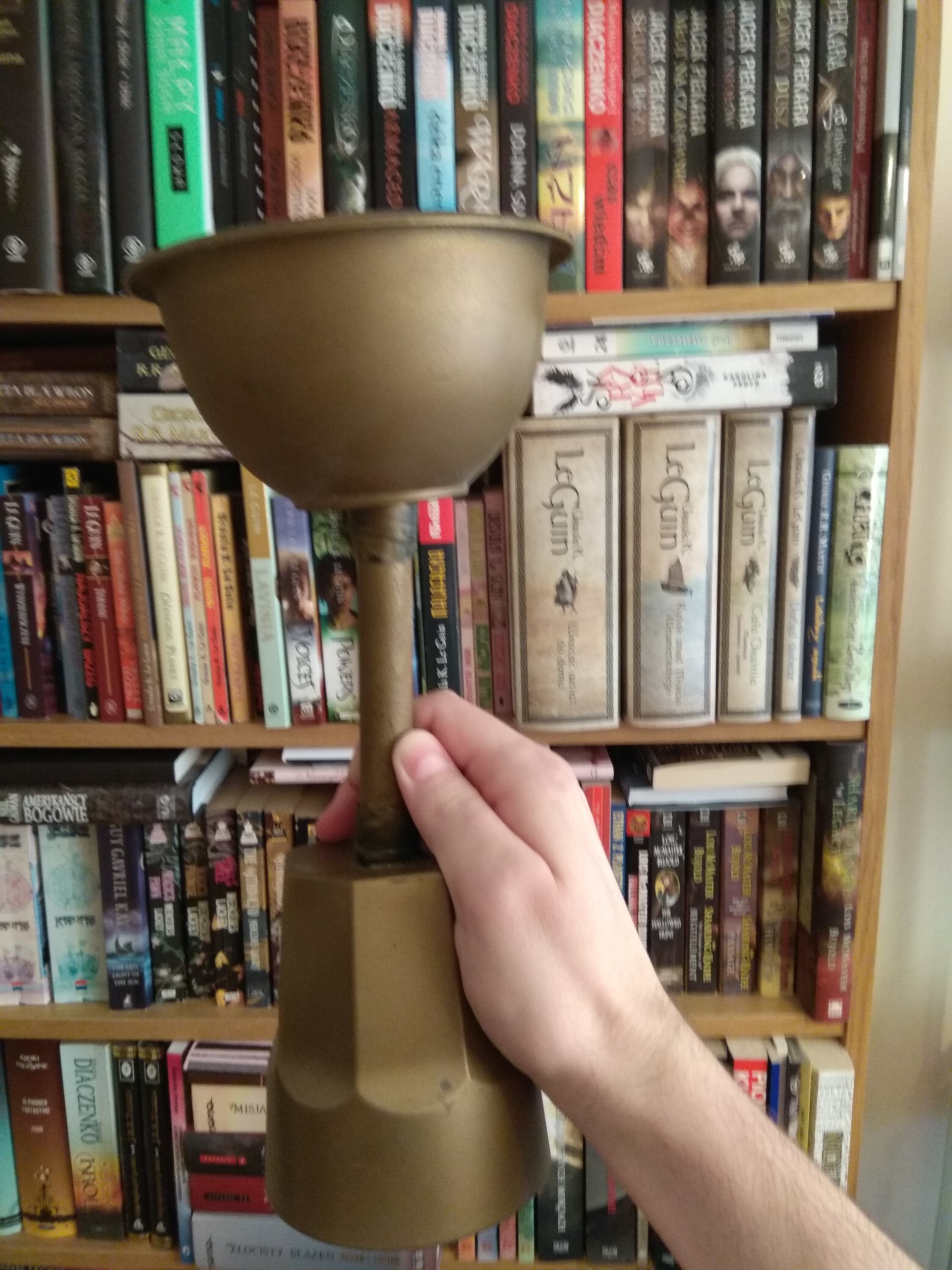 Hand holding a golden cup in front of the bookshelf.