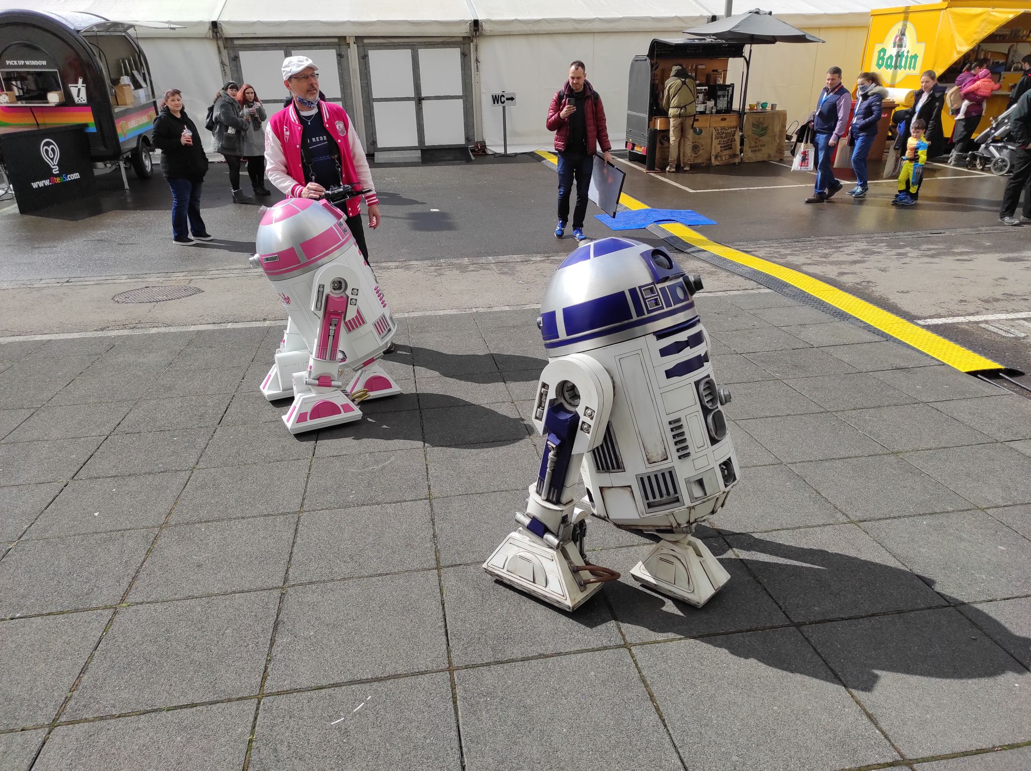 Two droids on a concrete pavement. The first one has blue and the othe rpink elements.