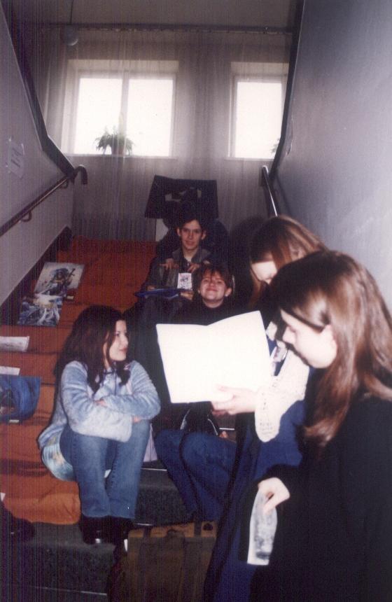 A group of people sitting on the stairs. There are some pictures laying on the stairs too.