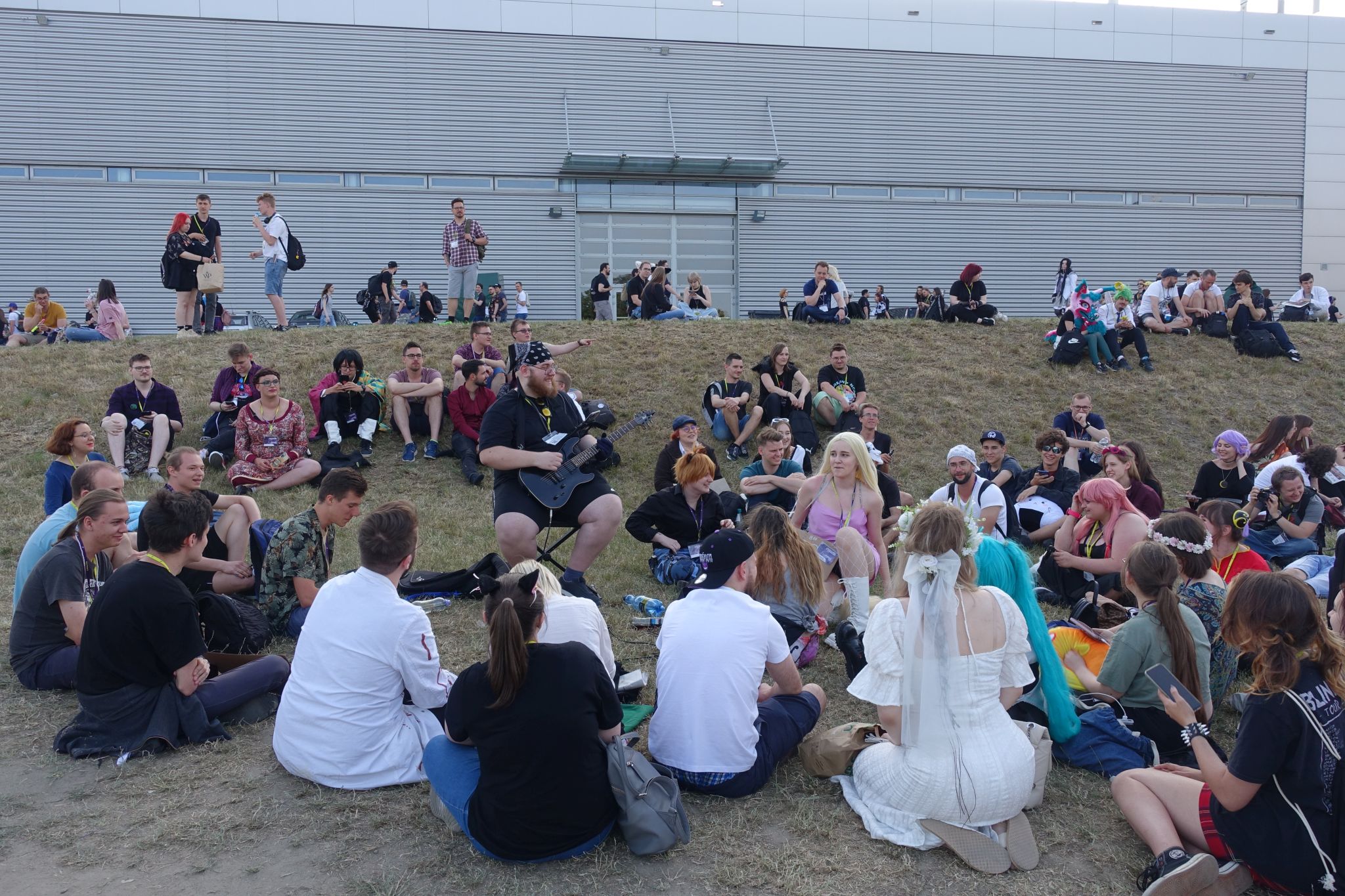 Picture was taken outdoors and shows a group of people surrounding a man playing the guitar.