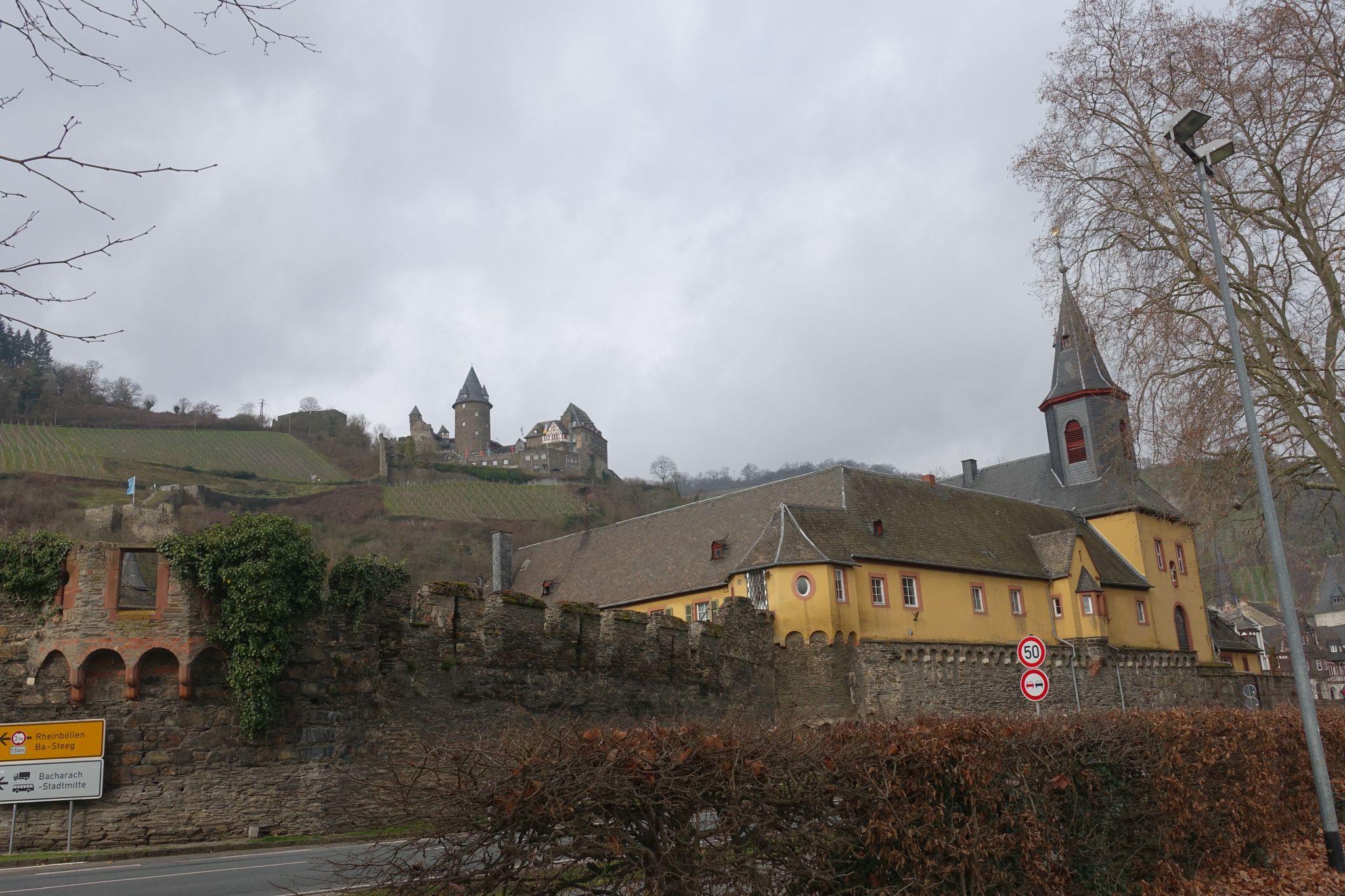 A picture shows old city walls with a church using them as one of the walls. In the background there is a castle on a hill.