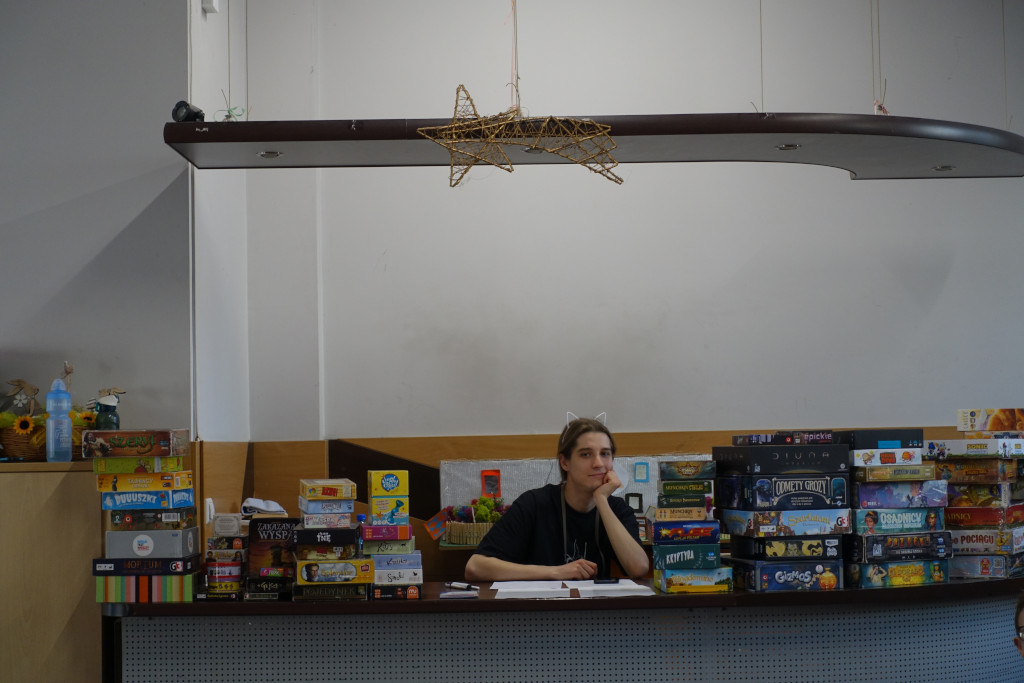 A person with cat ears sitting behind a desk. There are multiple board games on the desk.
