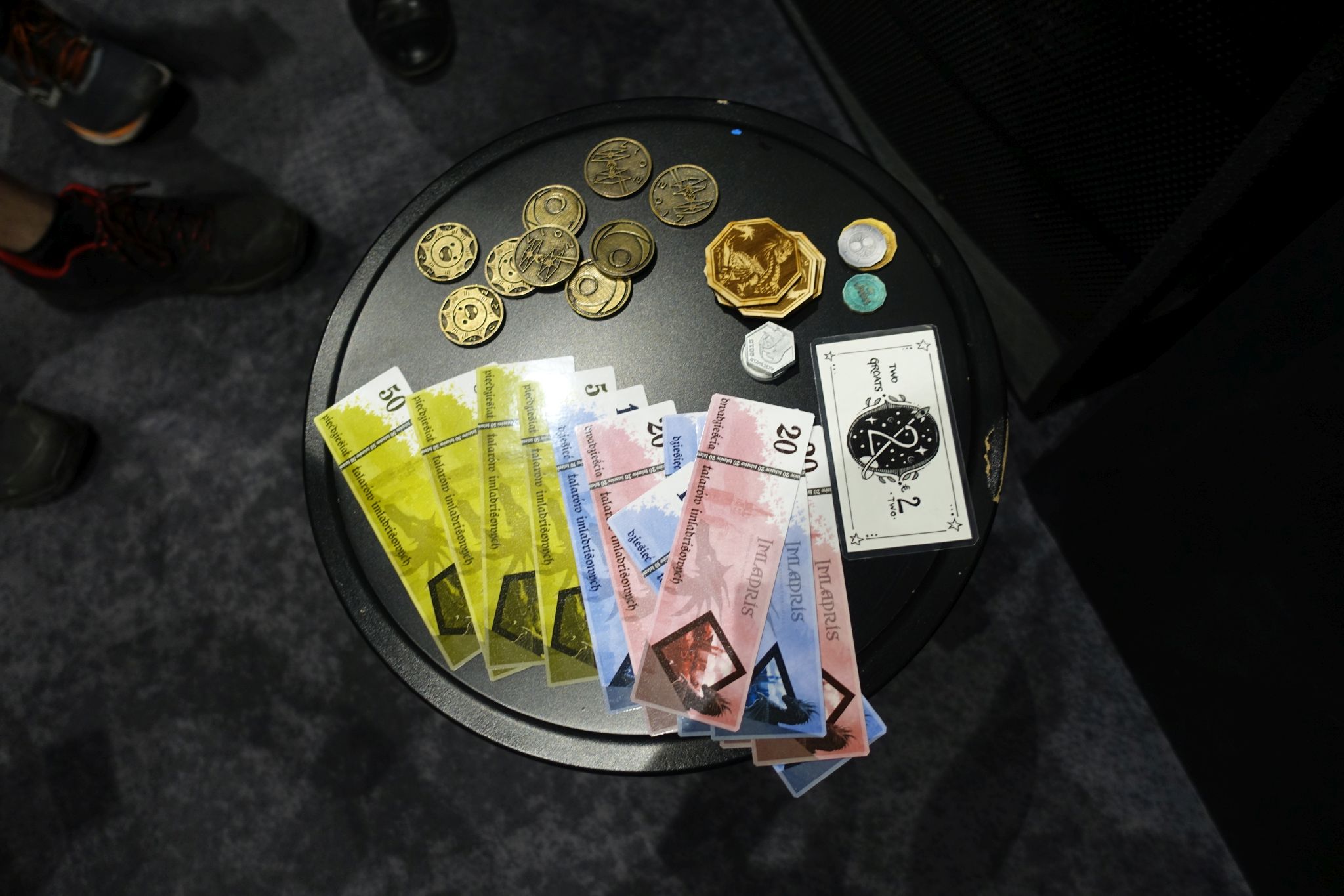 Picture shows multiple kinds of 'currency' on a stool. There are coins (metal and carton ones) and notes.