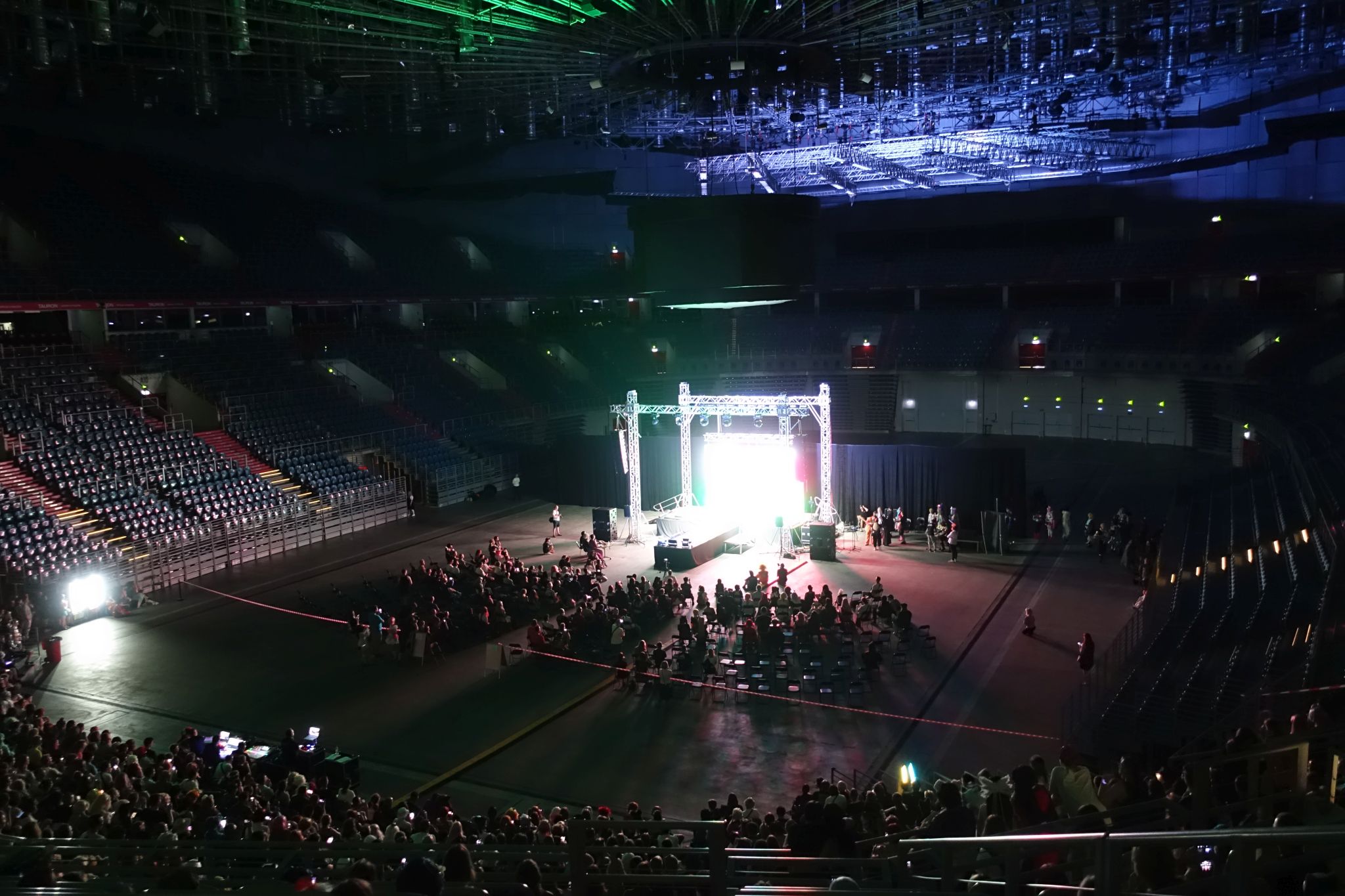 A picture showing a stage surrounded by the stands. On the stage there is a big and very bright screen.