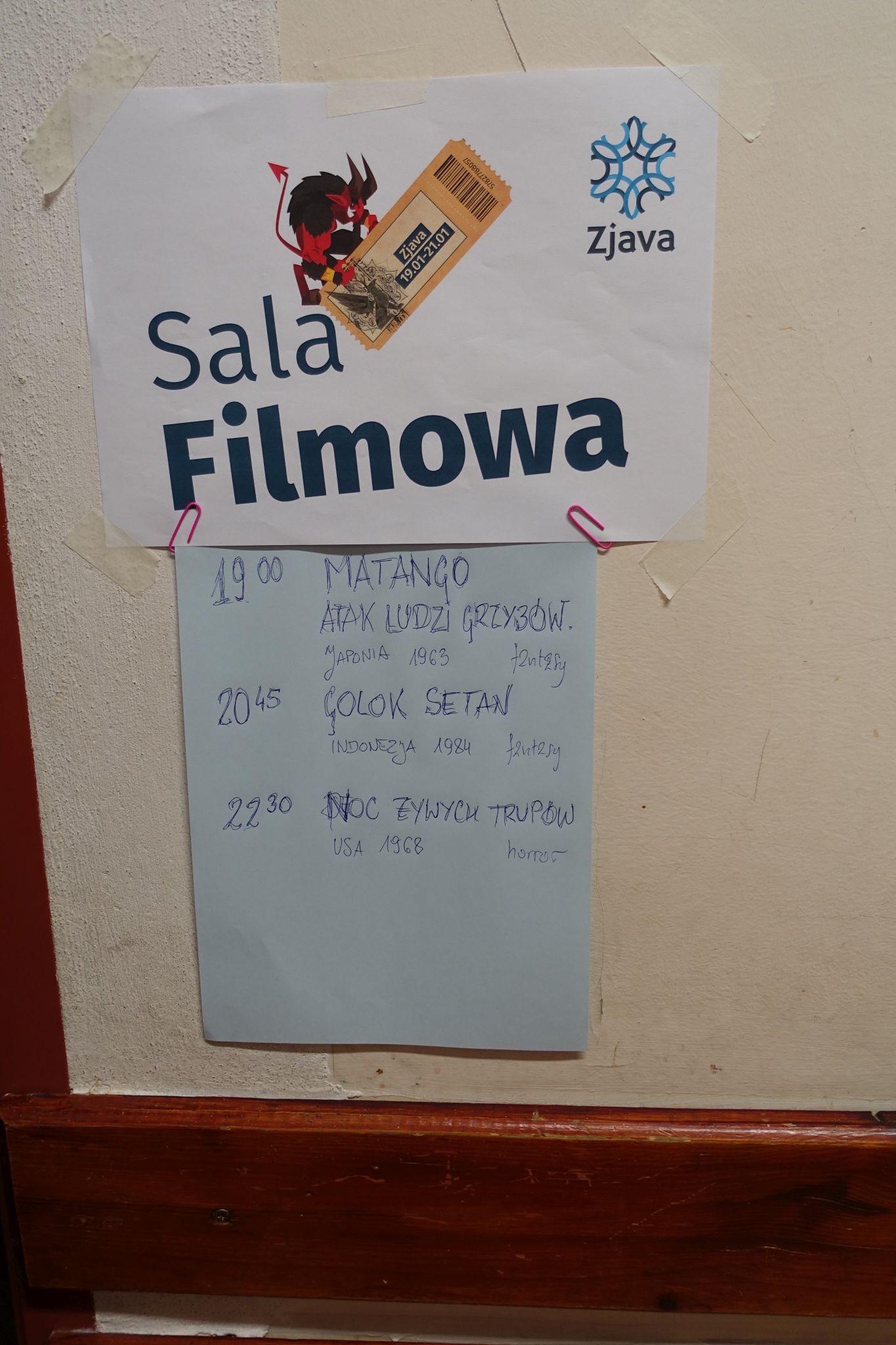 Two sheets of paper glued to a wall. the first is nicely printed and reads 'Zjava Sala Filmowa'. The second one below is written with a pen and lists three movies that will be screened.